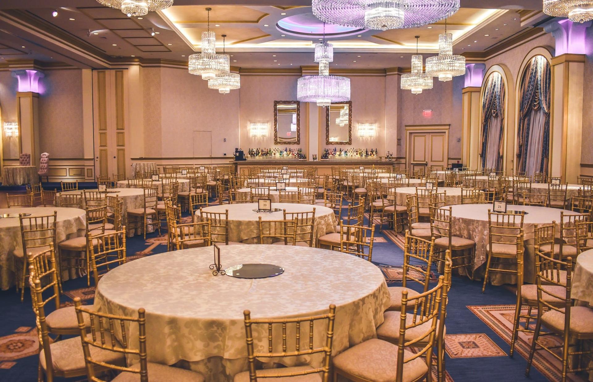 A chandelier-lit ballroom prepared with round tables and gold chairs