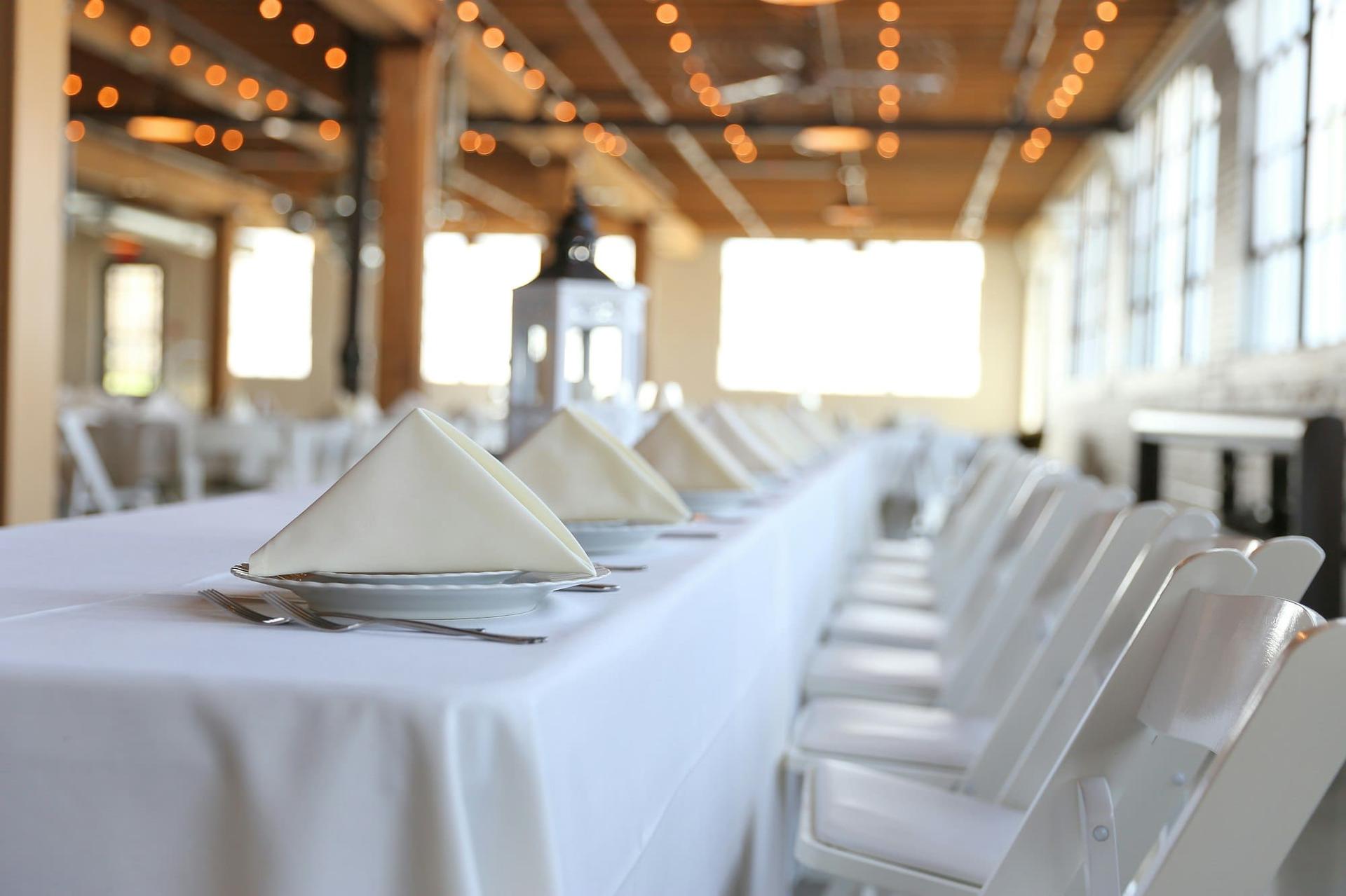A long banquet table set with folded napkins in a bright venue