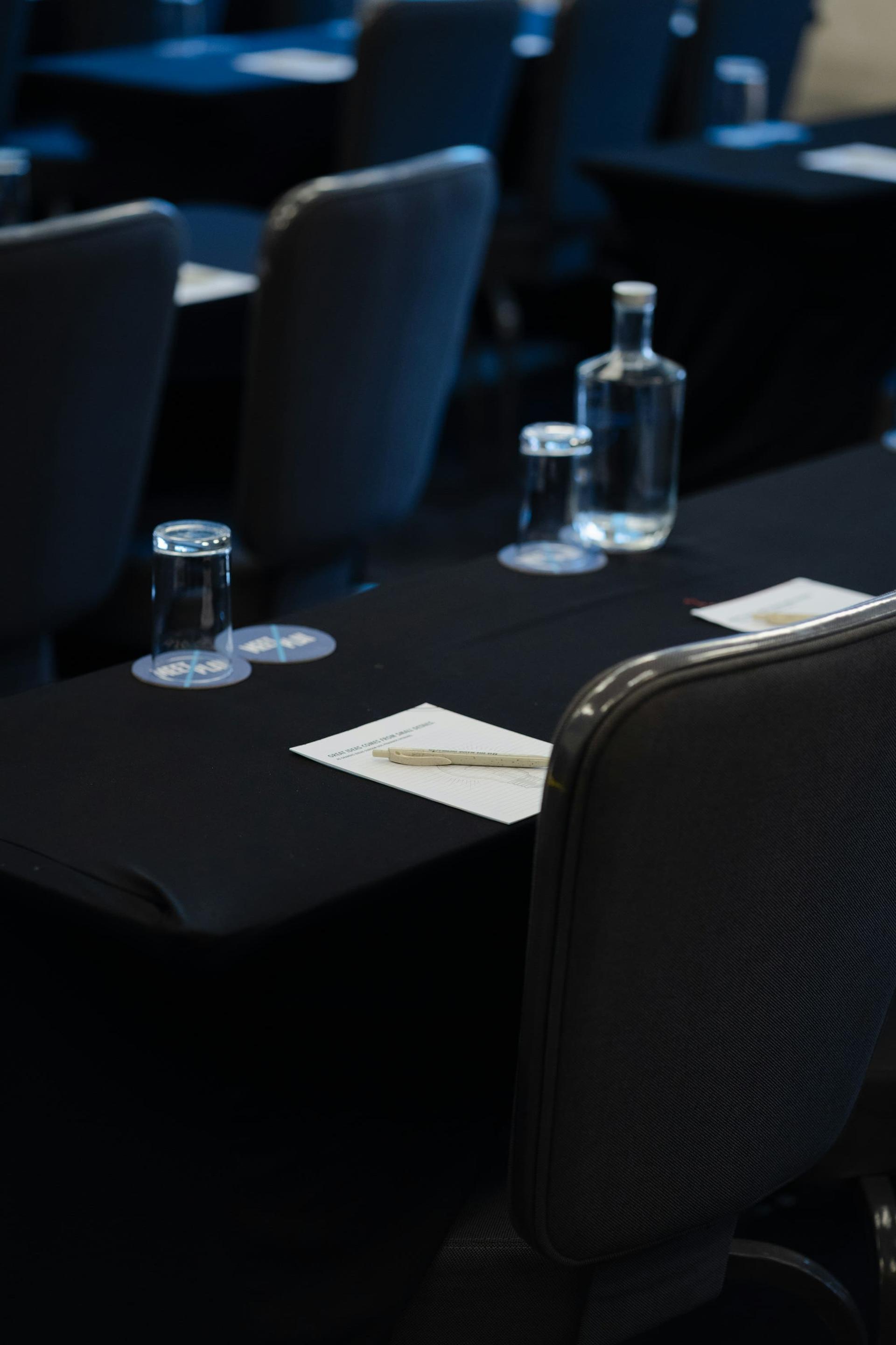 Conference tables dressed in black linen with water, glasses and notepads