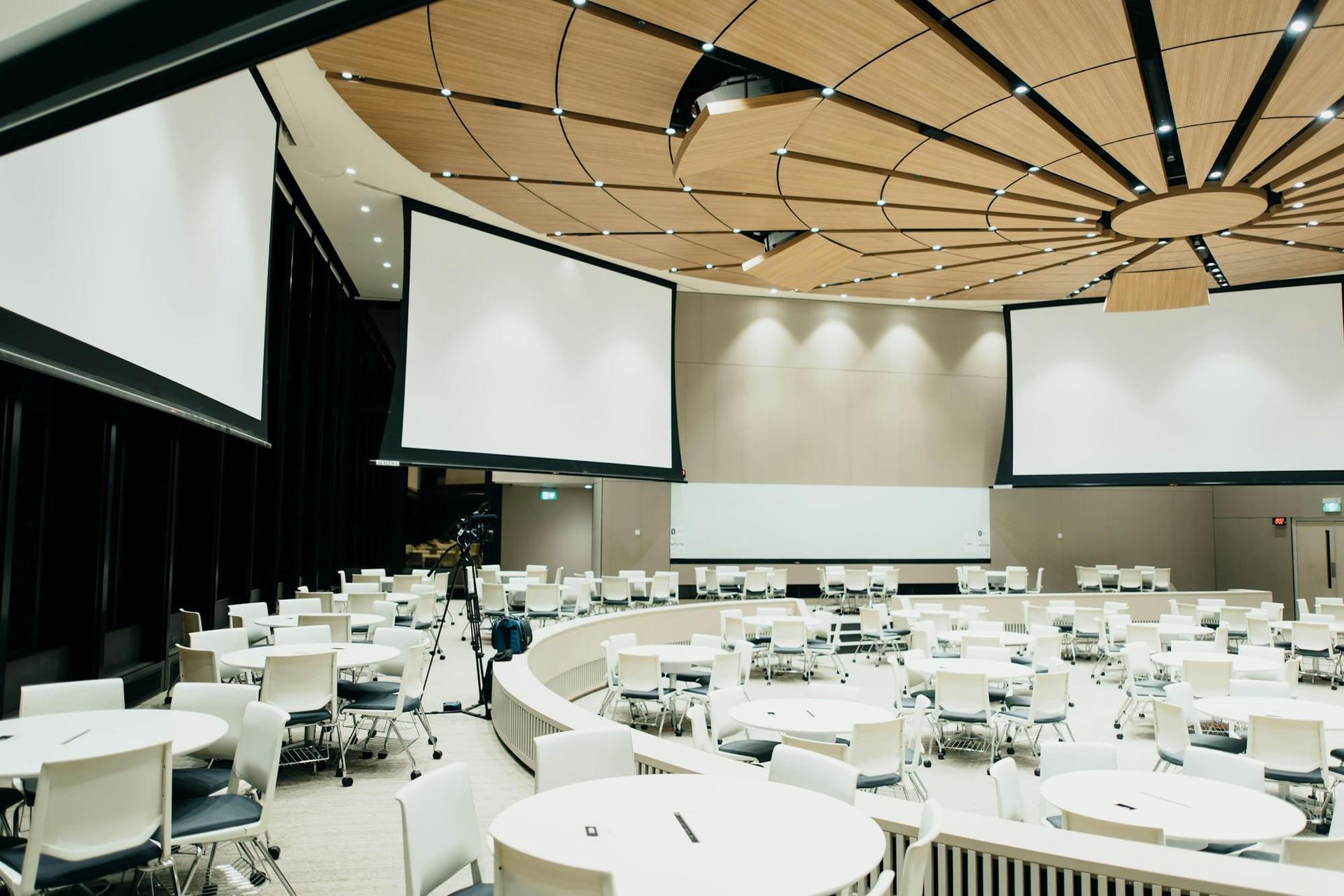 A conference venue with round tables and three projection screens