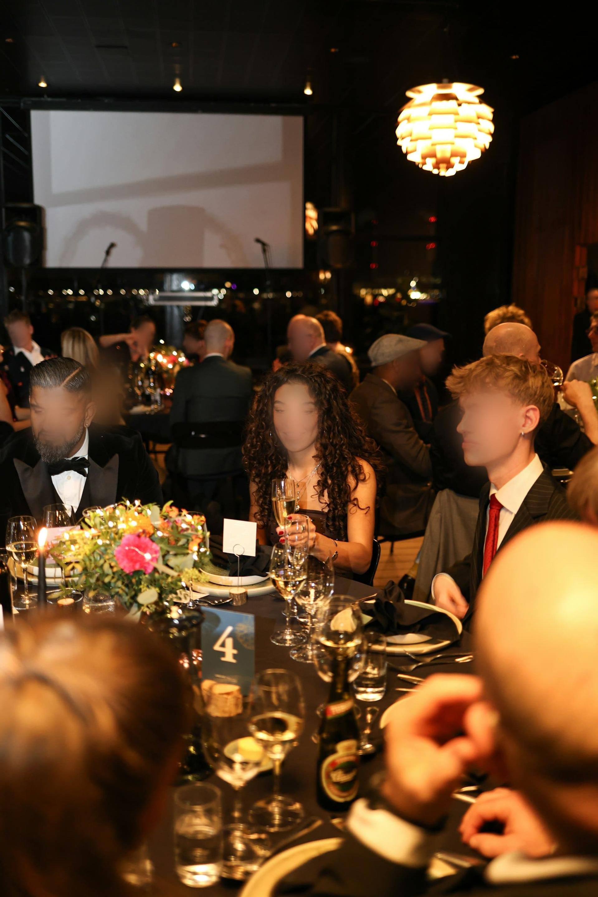 Guests in black tie seated at a candlelit gala dinner with floral centrepieces