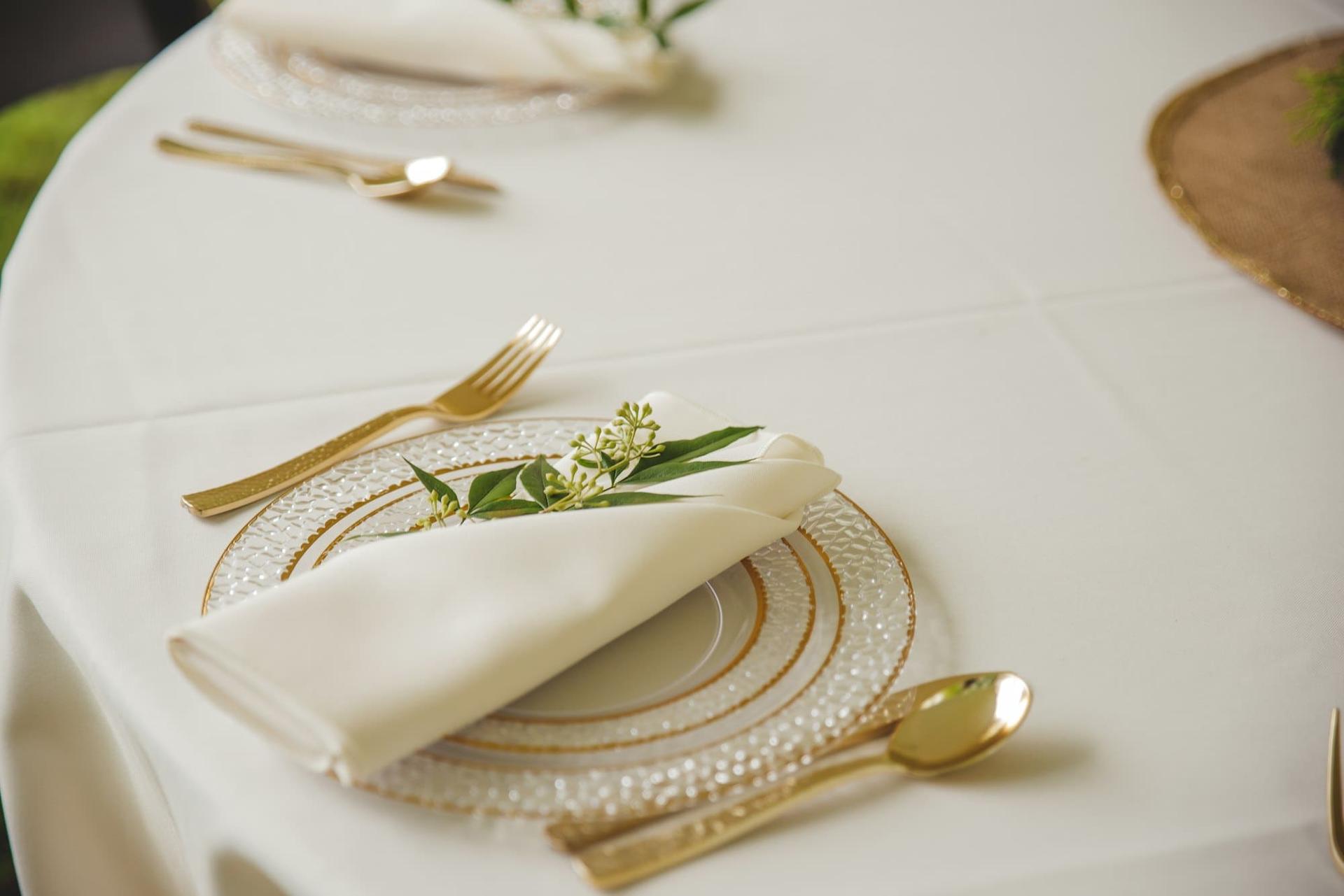 A place setting with gold cutlery, a folded napkin and a sprig of greenery