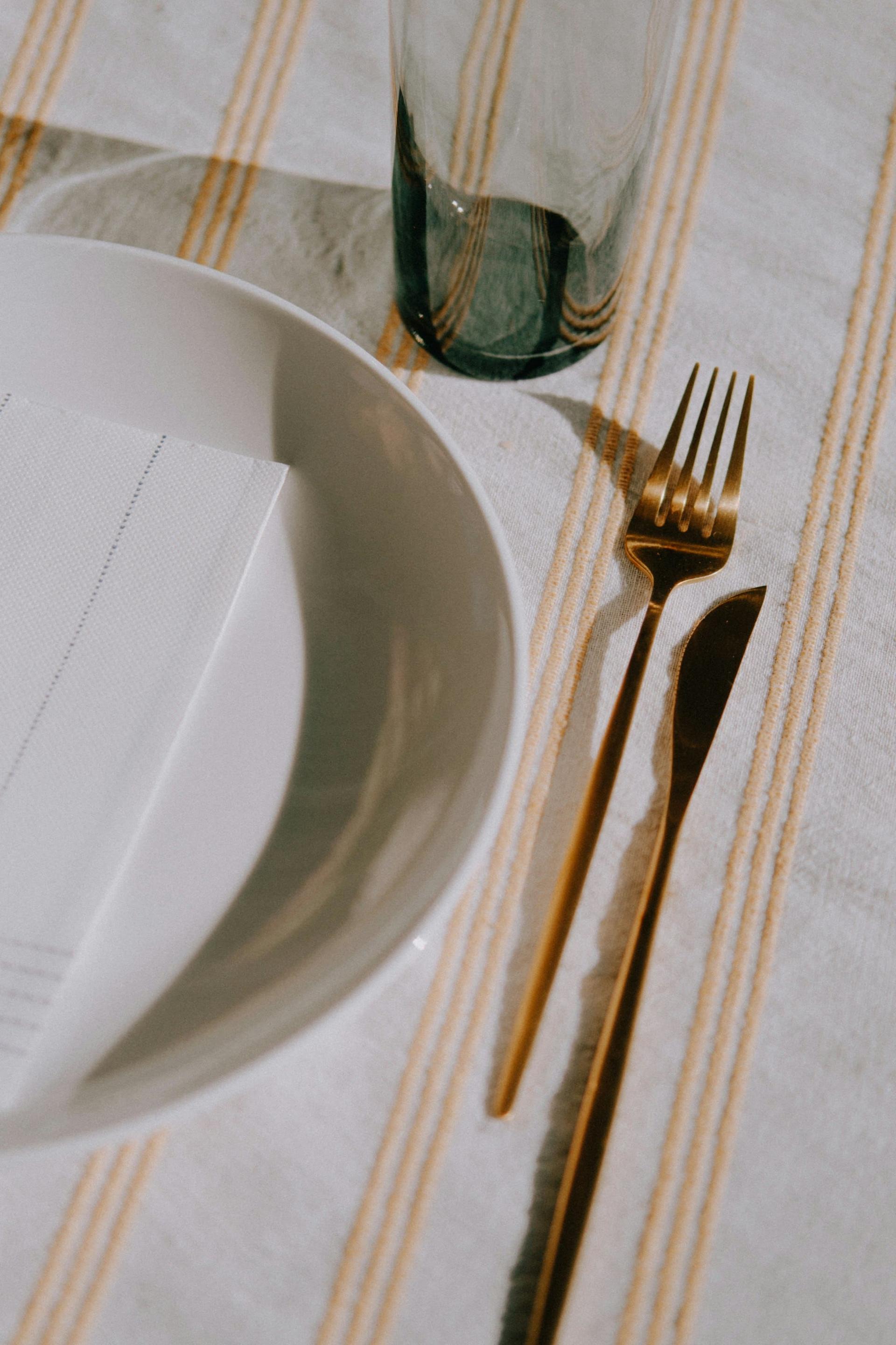 Gold flatware beside a white plate on striped linen