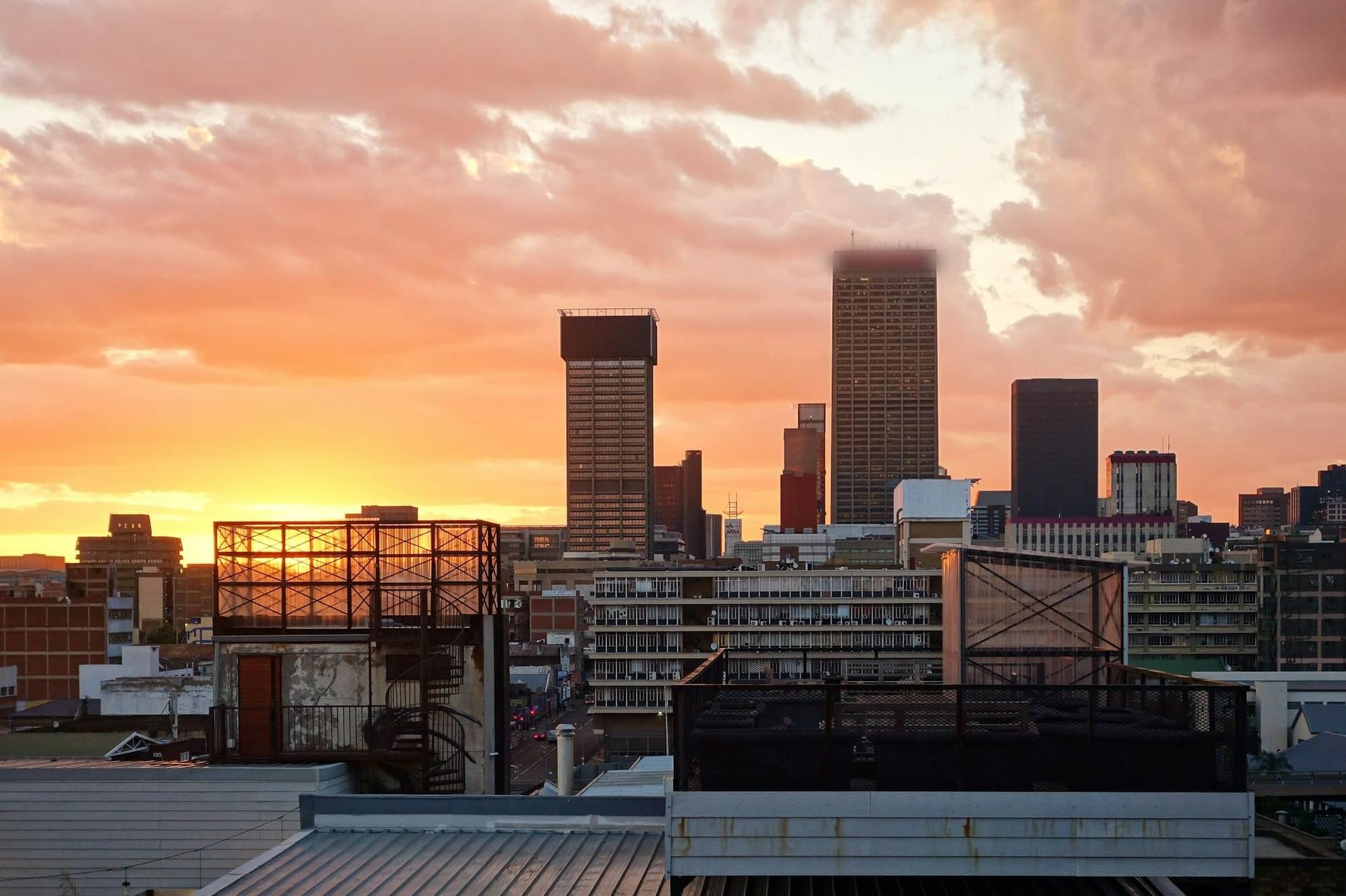 City towers against a pink and orange sunset, seen across rooftops and a water tank
